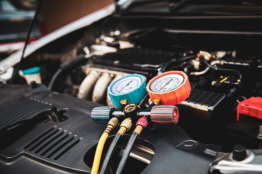 auto mechanic using measuring manifold gauge to check vehicle refrigerant for air conditioner system